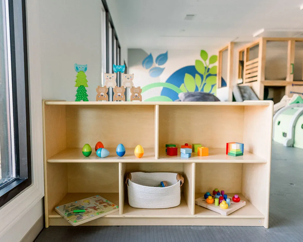 Wooden toy shelf filled with stacking bears, blocks, and plastic eggs in the indoor playroom