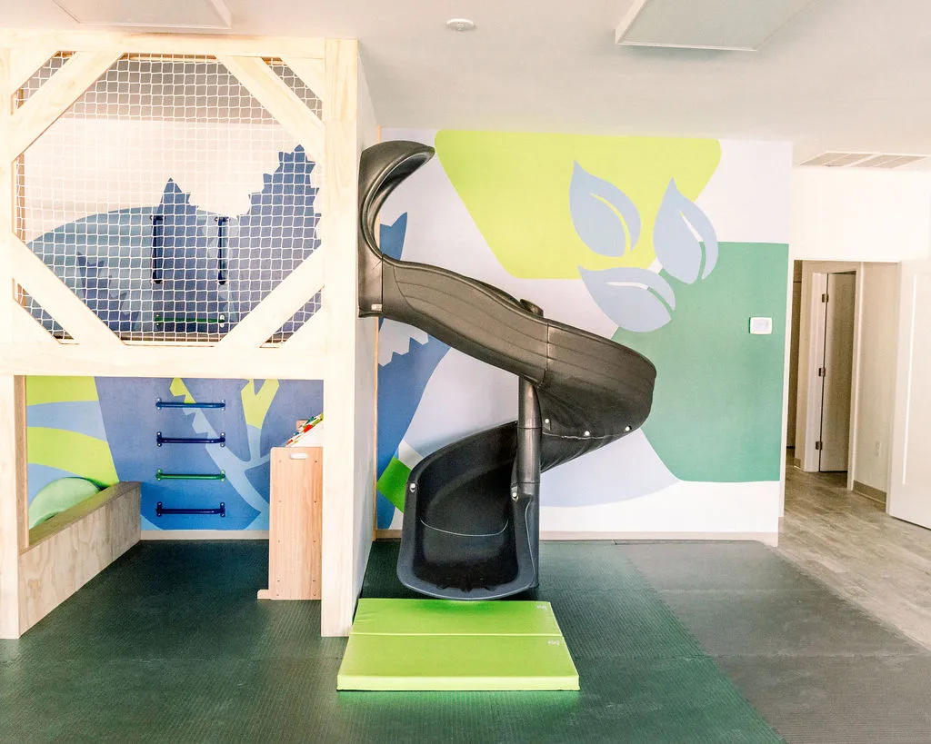 Black spiral slide with a lime green landing mat next to a wooden climbing structure