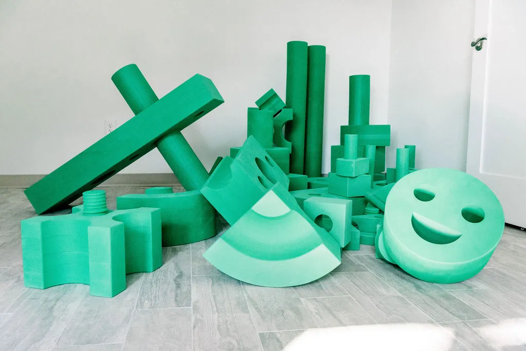 Bright green foam play blocks in assorted shapes piled on a grey wood-patterned floor