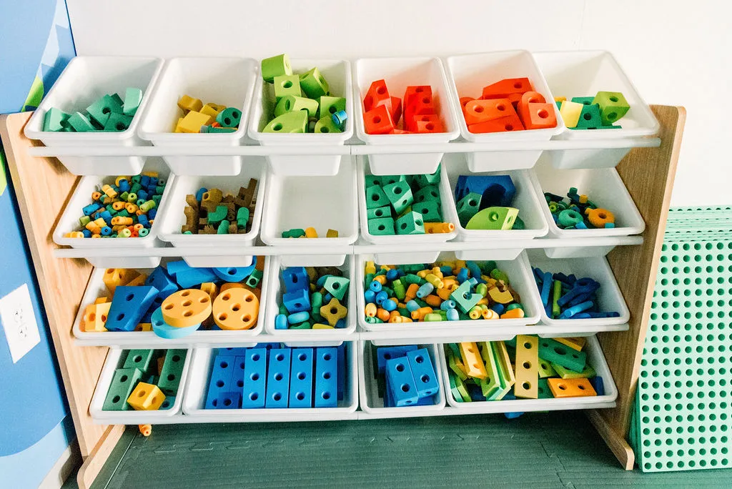 Wooden shelving unit holding bins of colorful plastic building blocks and connectors