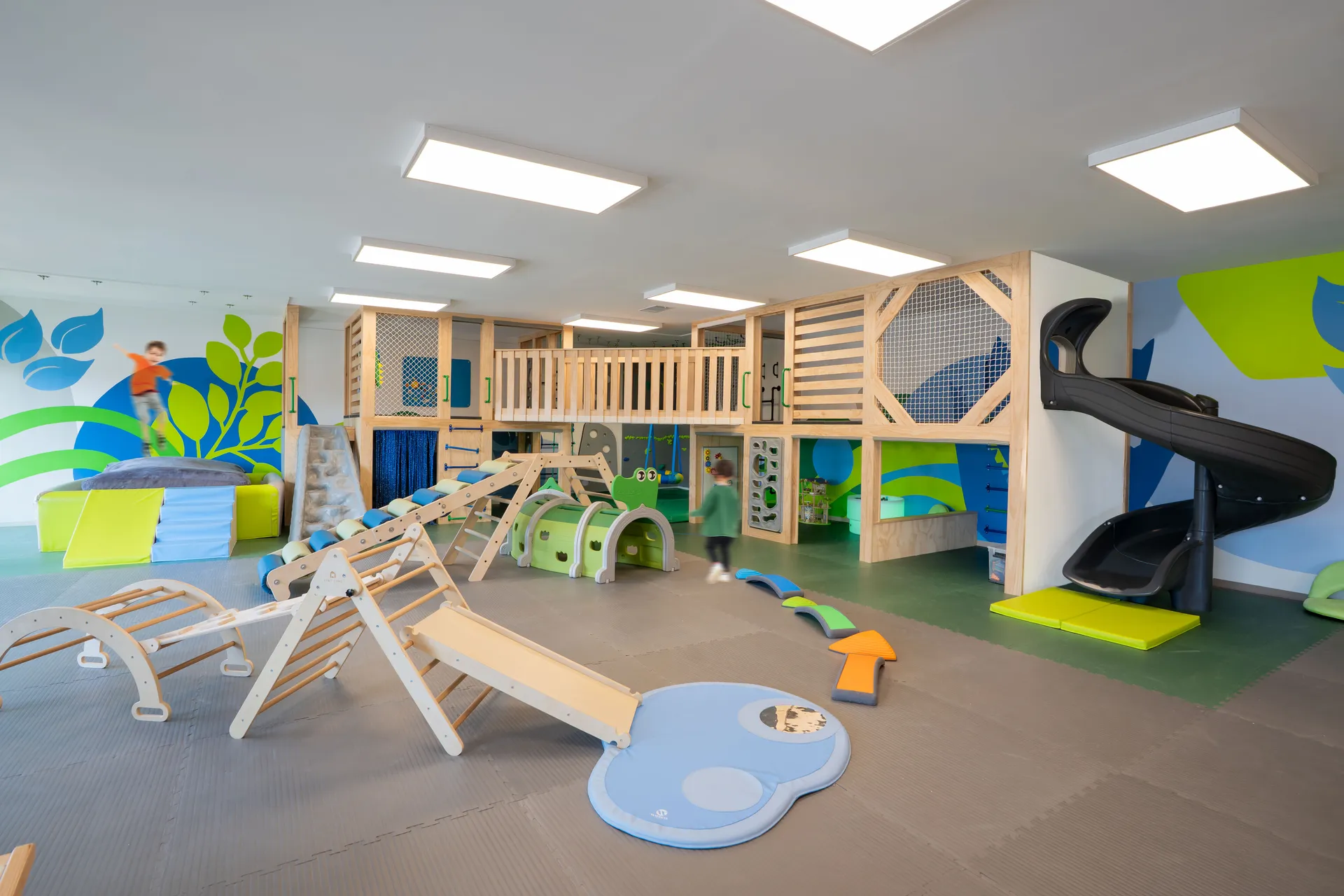 Children playing on a large wooden multi-level structure with a spiral slide and climbing equipment